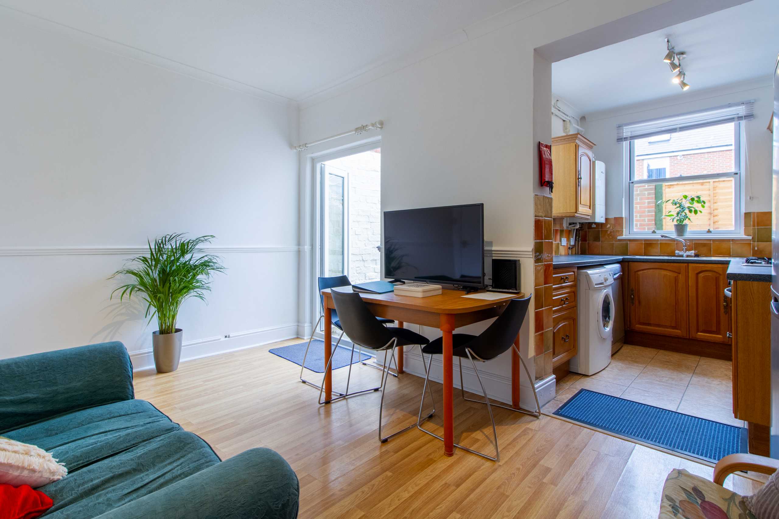 Open-plan living and dining area with a sofa, television, dining table and chairs, leading into a fitted kitchen.