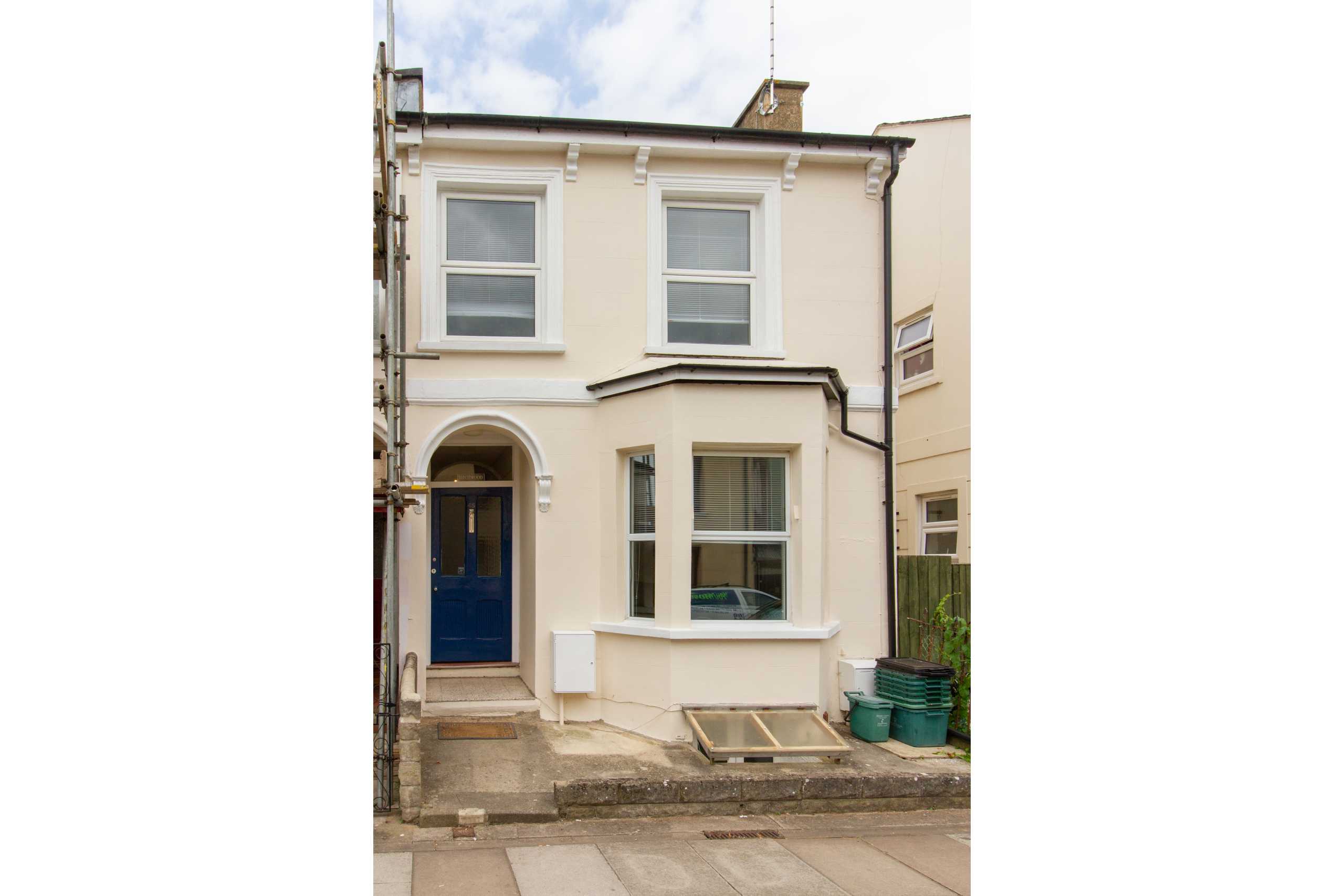 Front exterior of a narrow two-storey terraced house with cream walls, white-framed windows and a blue front door.