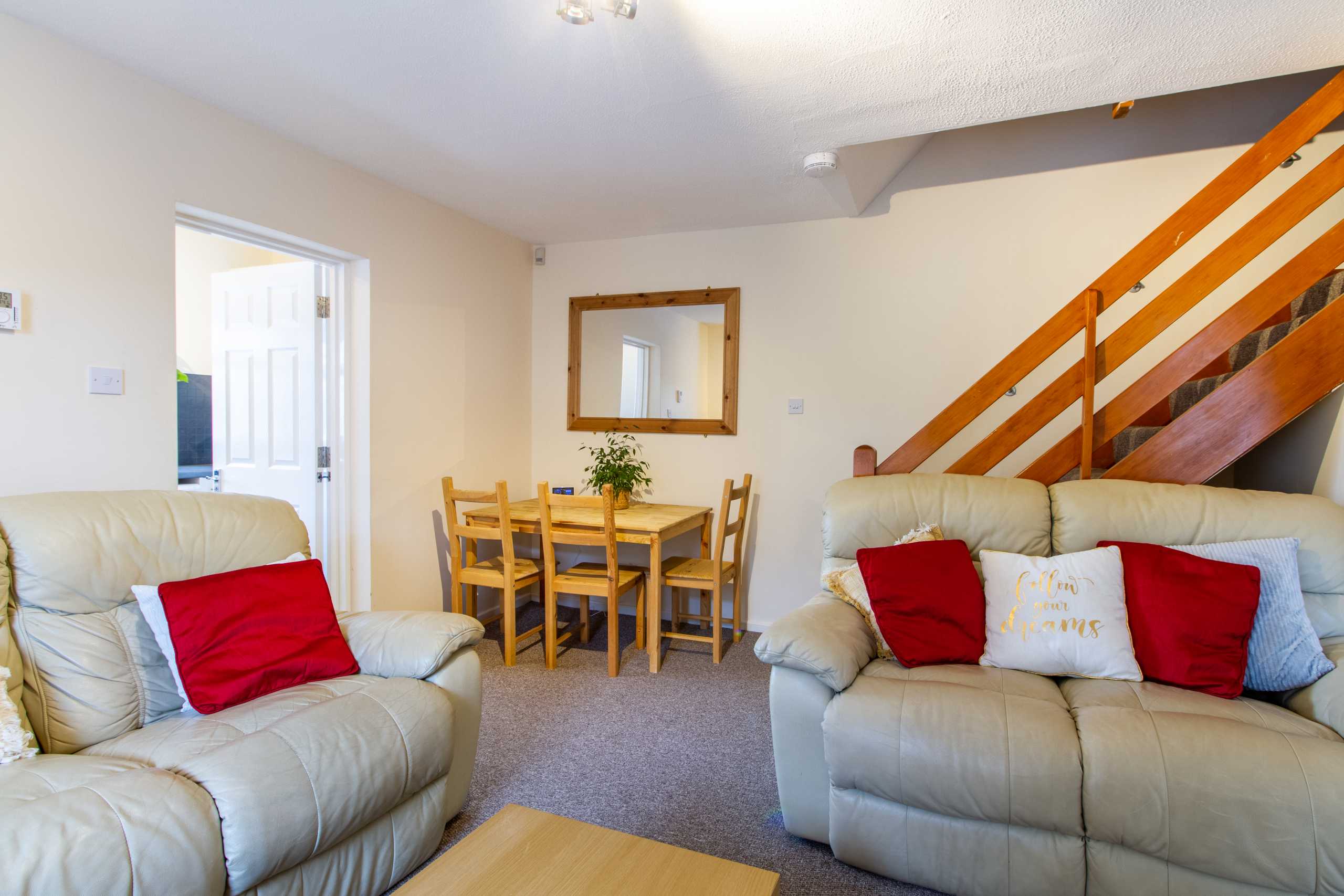 Living room and dining area with sofas, a dining table, and a wooden staircase.