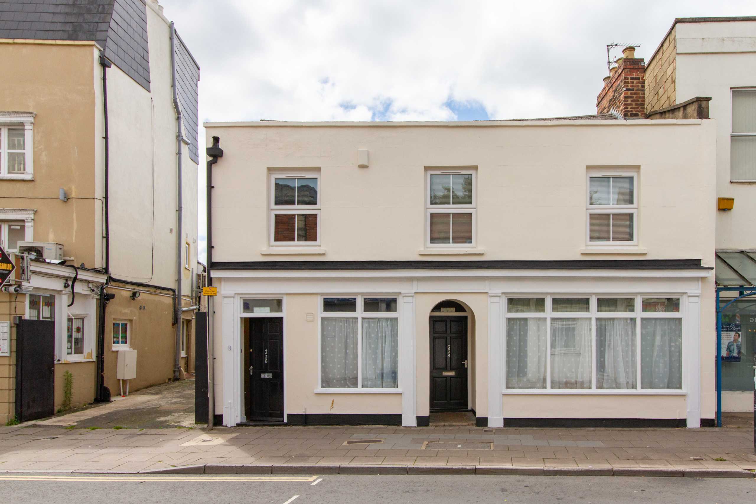 Front exterior of a two-storey terraced residential building with windows, doors and pavement.