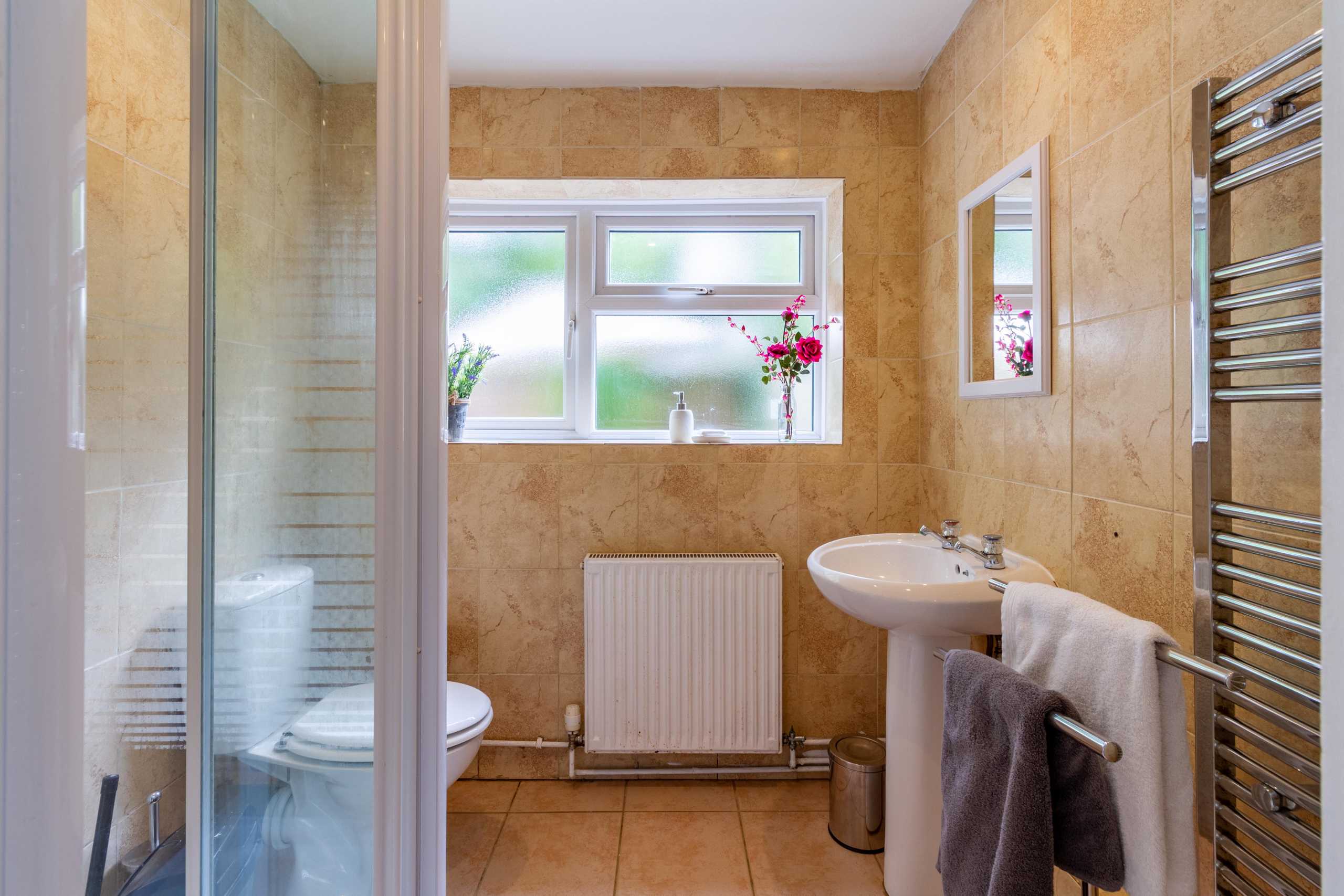 Bathroom with a shower enclosure, toilet, pedestal sink, window, radiator and heated towel rail.