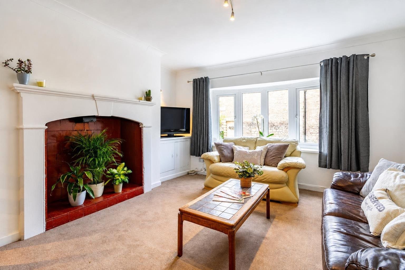 Bright living room with a fireplace, seating, coffee table, television and large bay window.
