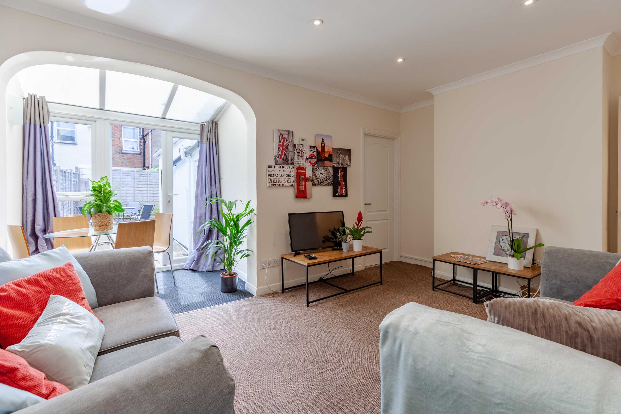 Bright living room with sofas, coffee tables, a television, plants and a large arched window.