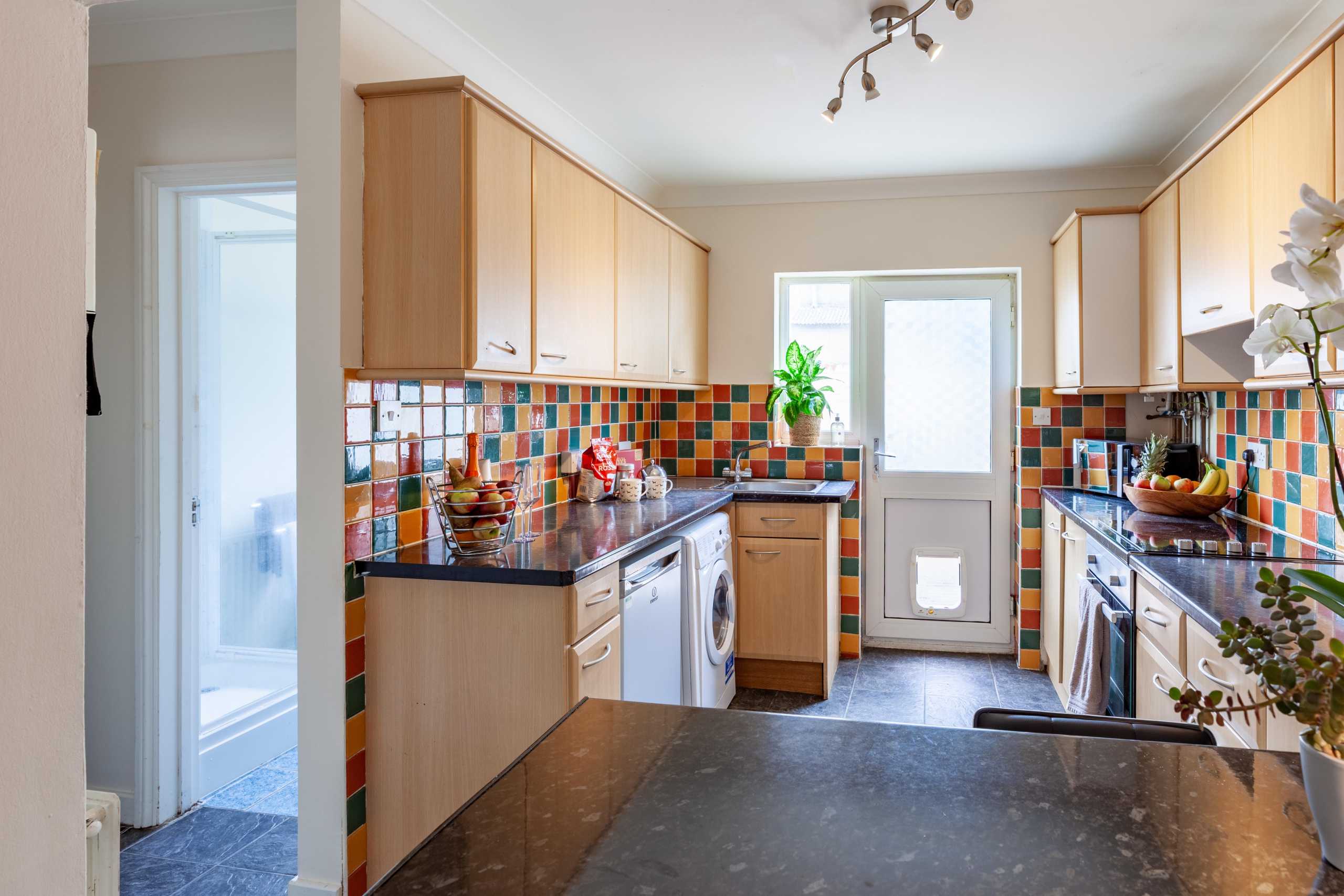Bright fitted kitchen with wooden cabinets, colorful tiled backsplash, appliances, and a rear door.