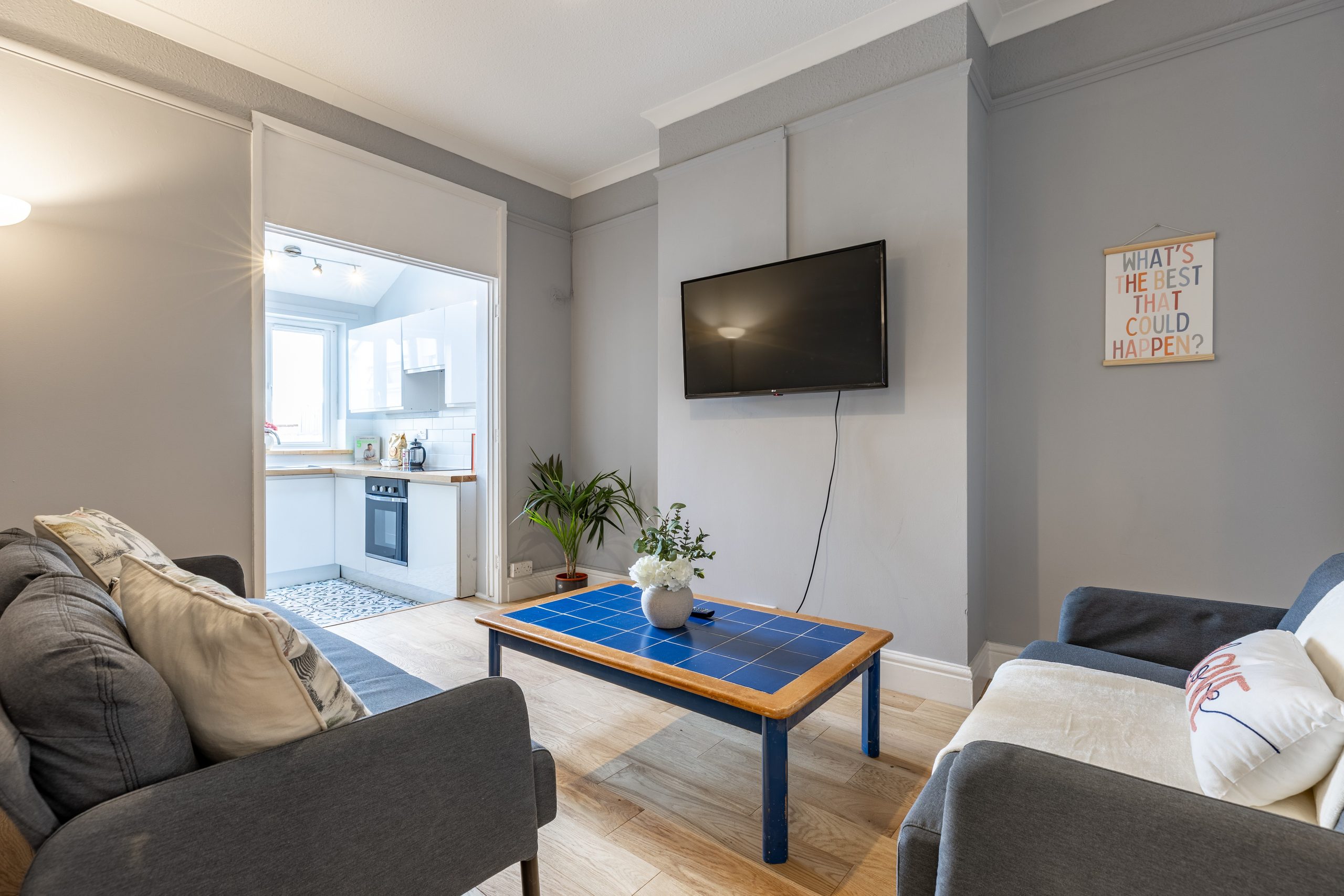 Furnished living room with sofas, a wall-mounted television, coffee table and open doorway to a kitchen.
