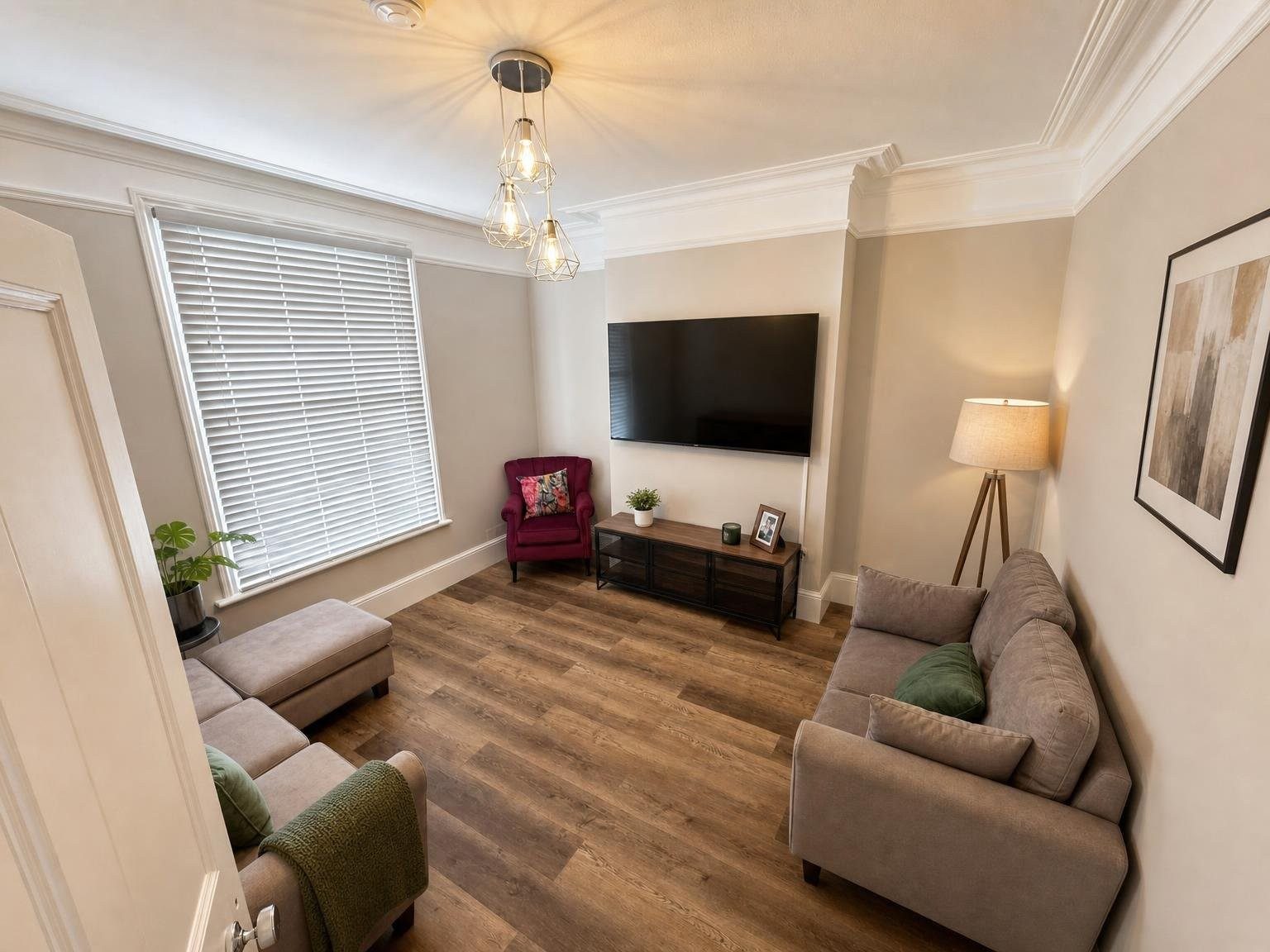 Furnished living room with sofas, an armchair, television, window blinds and wood-effect flooring.