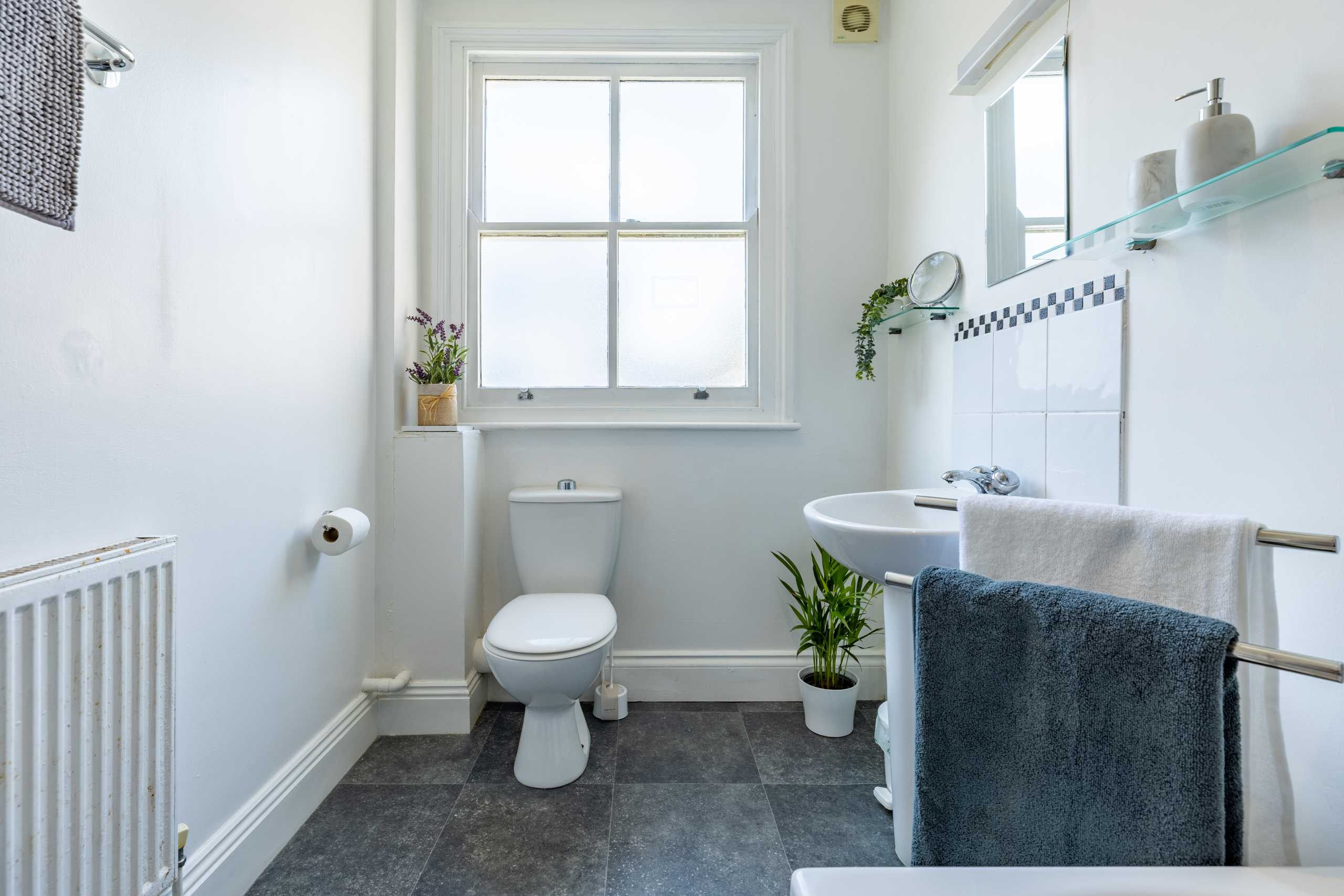 Bright bathroom with a toilet, sink, bathtub, window, radiator and tiled walls.